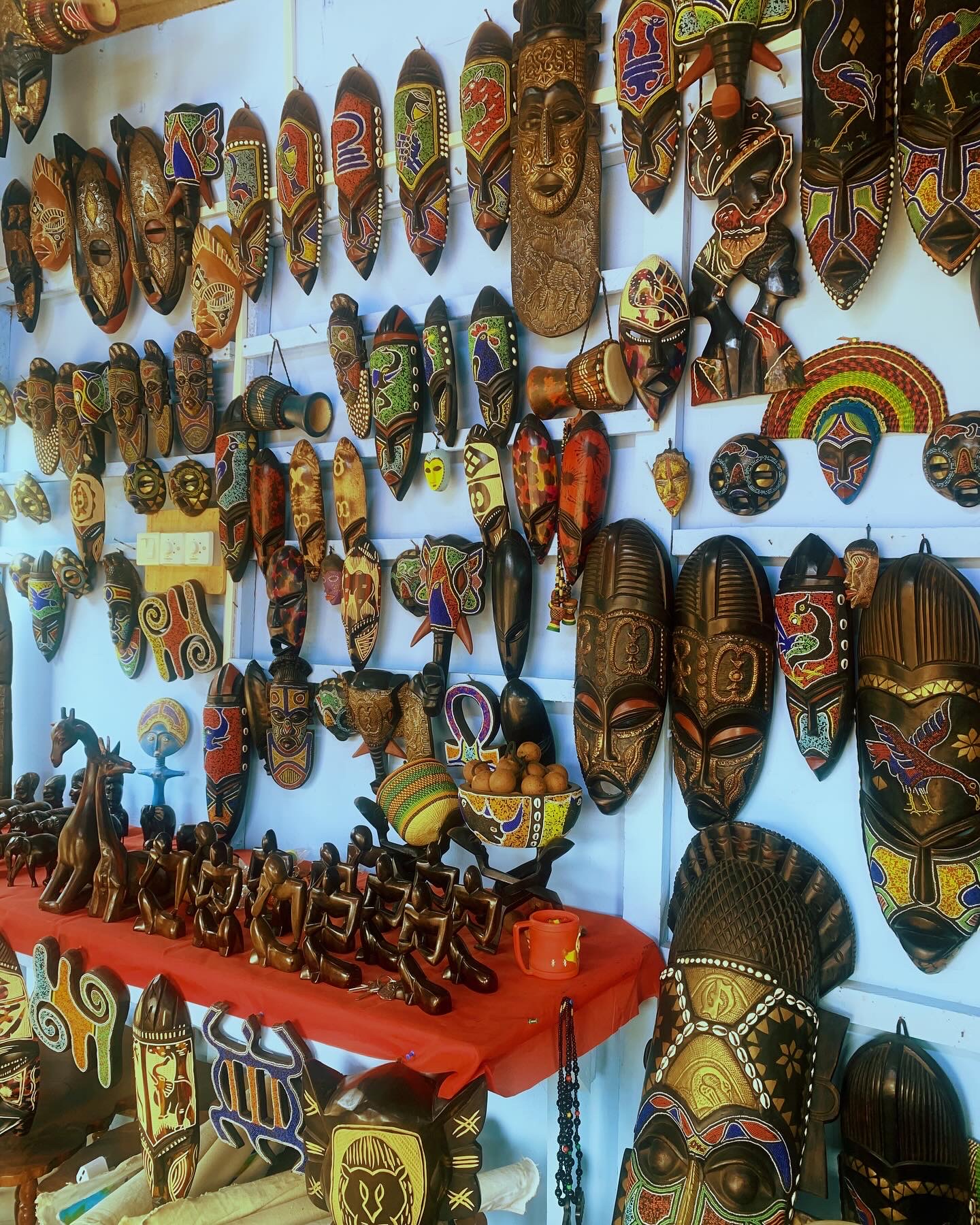 A wall and table filled with carved masks and objects