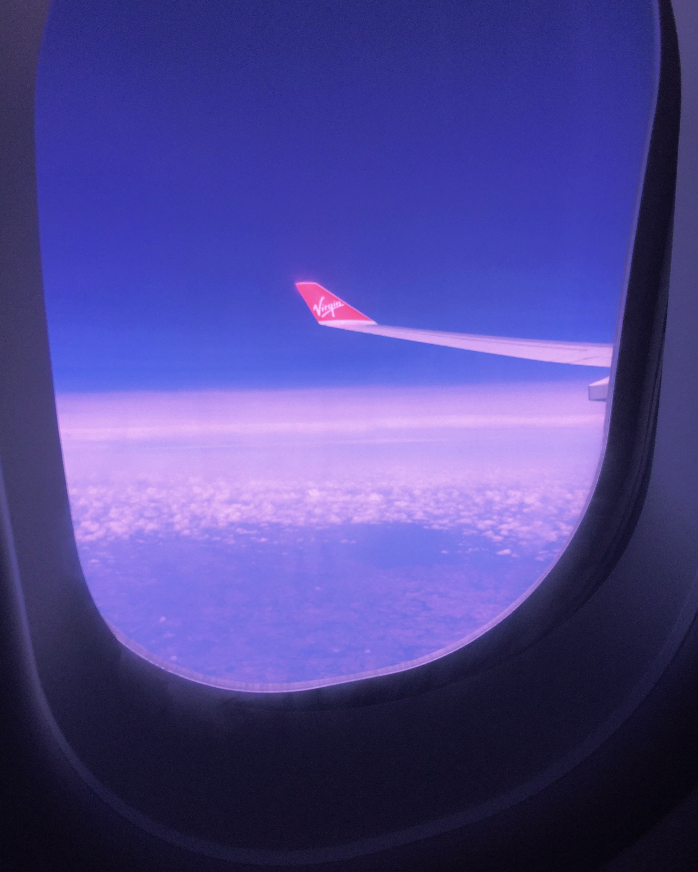 A plane wing above clouds seen through a window